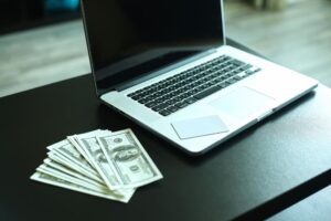 Computador na mesa com dinheiro, descubra Quanto ganha um desenvolvedor WEB freelancer